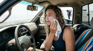 Woman removing mineral sunscreen from her face in a truck mirror at a beach parking lot