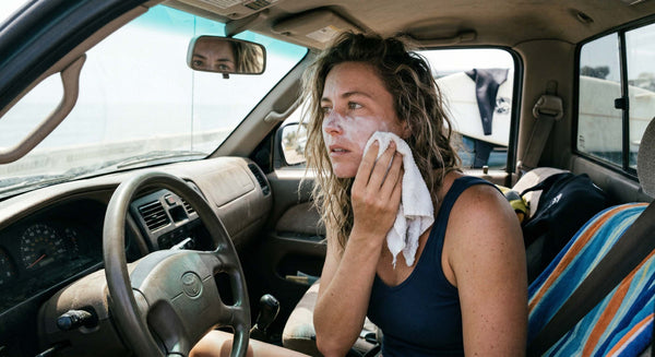 Woman removing mineral sunscreen from her face in a truck mirror at a beach parking lot